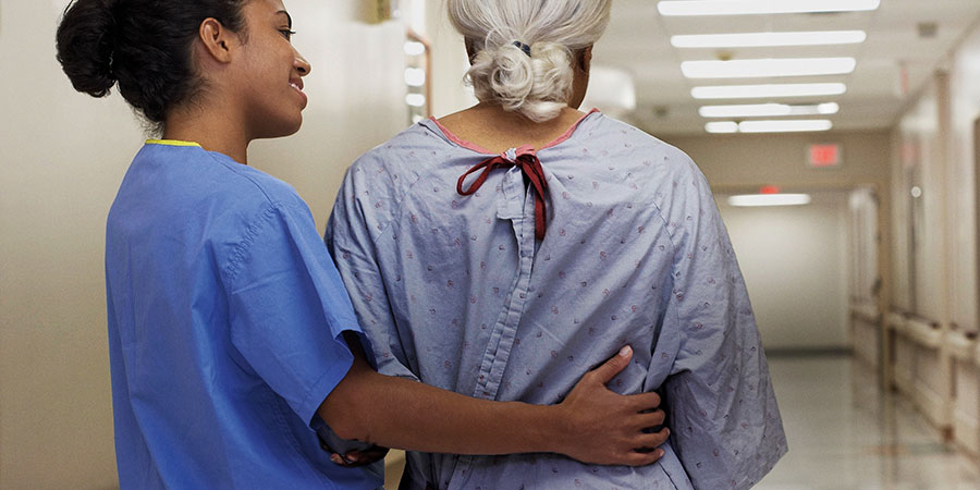 Photo of nurse helpinh a patient walk down hallway